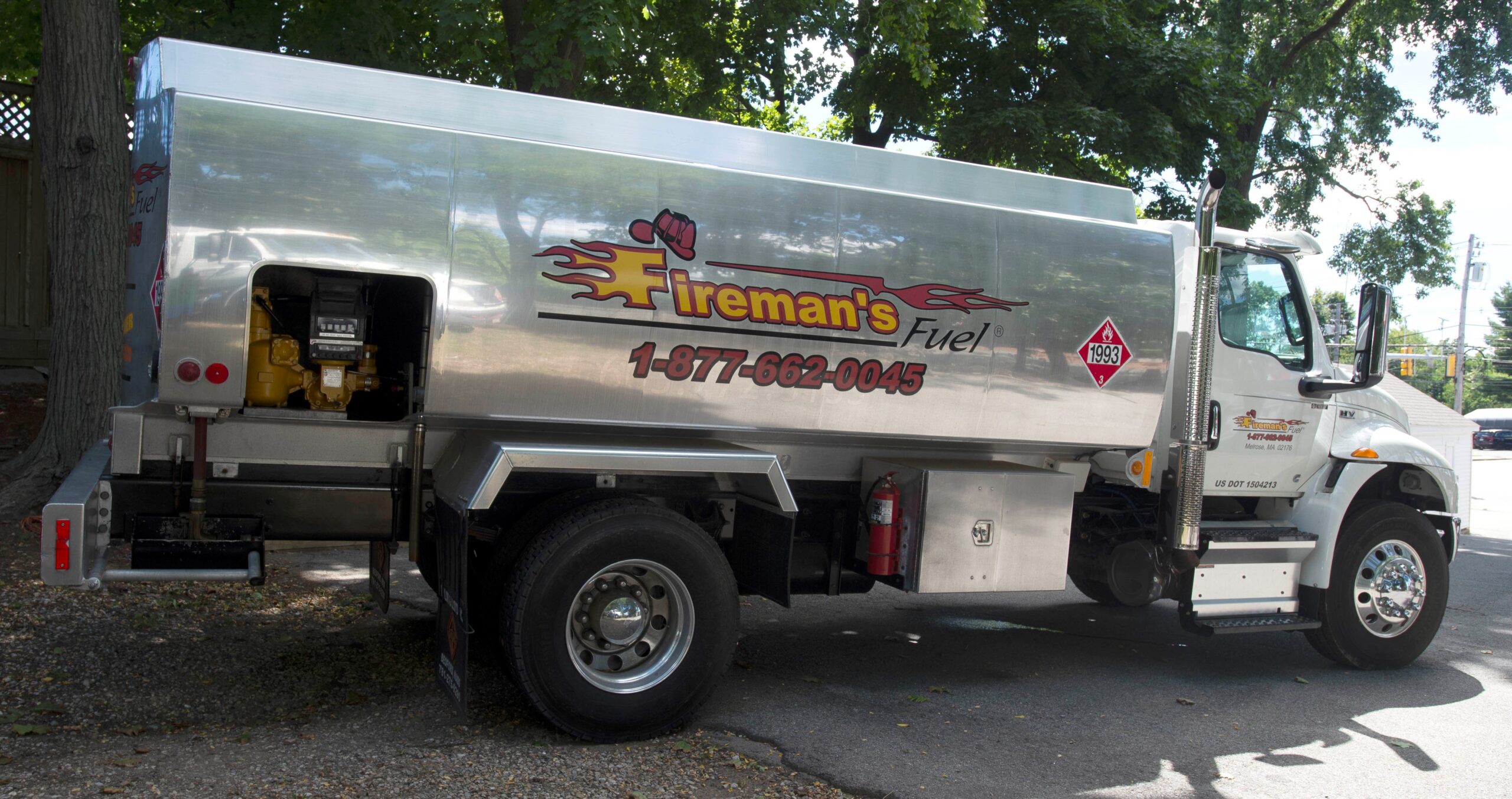 Fireman's Fuel stainless oil truck in profile under the trees